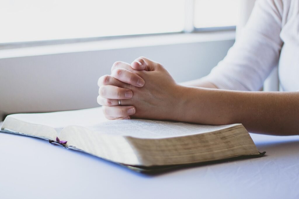 Folded hands praying over an open Bible